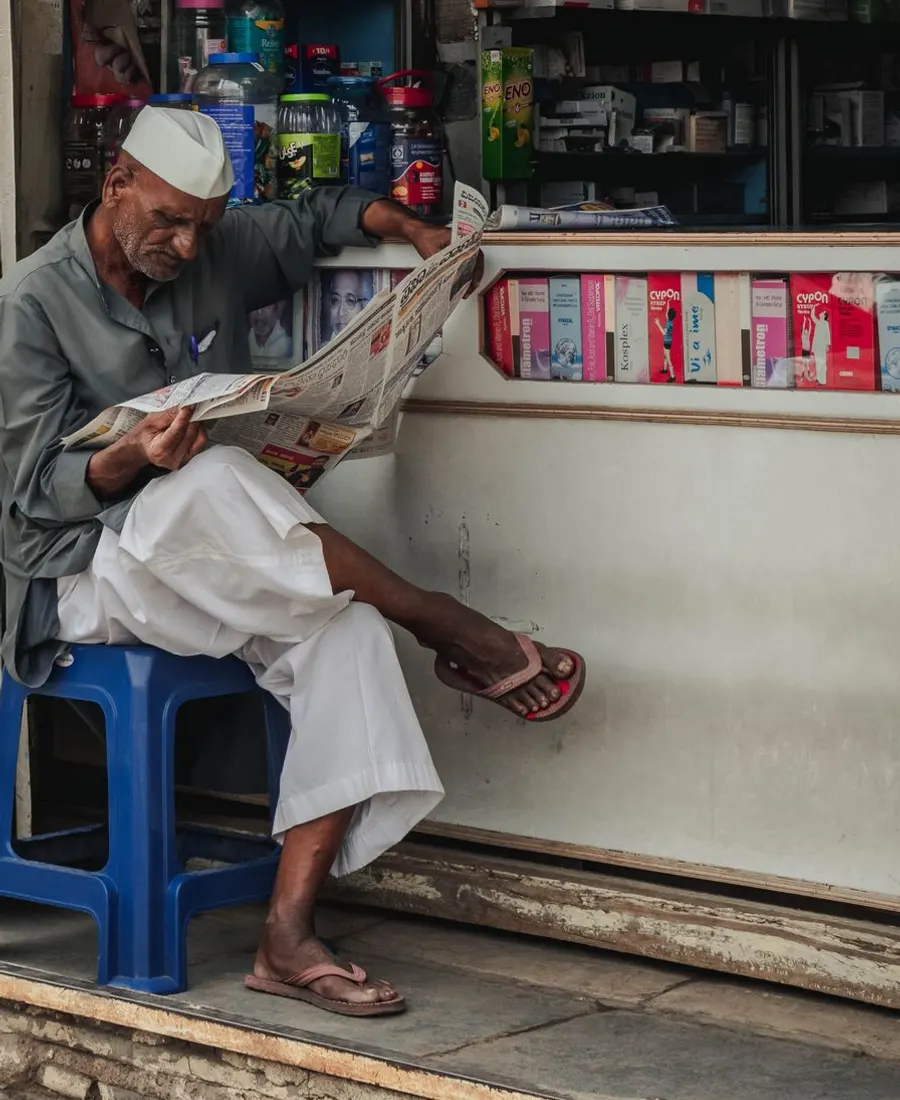 A man reading the newspaper outside a small medical shop in Karnataka